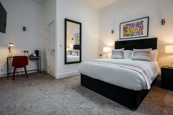 A bedroom with a large bed, a desk with a chair, a mirror, and artwork on the walls. - The Anfield Hotel (Liverpool)