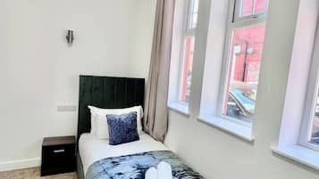 A bedroom with a bed, a nightstand, a window, and a view of the outside.