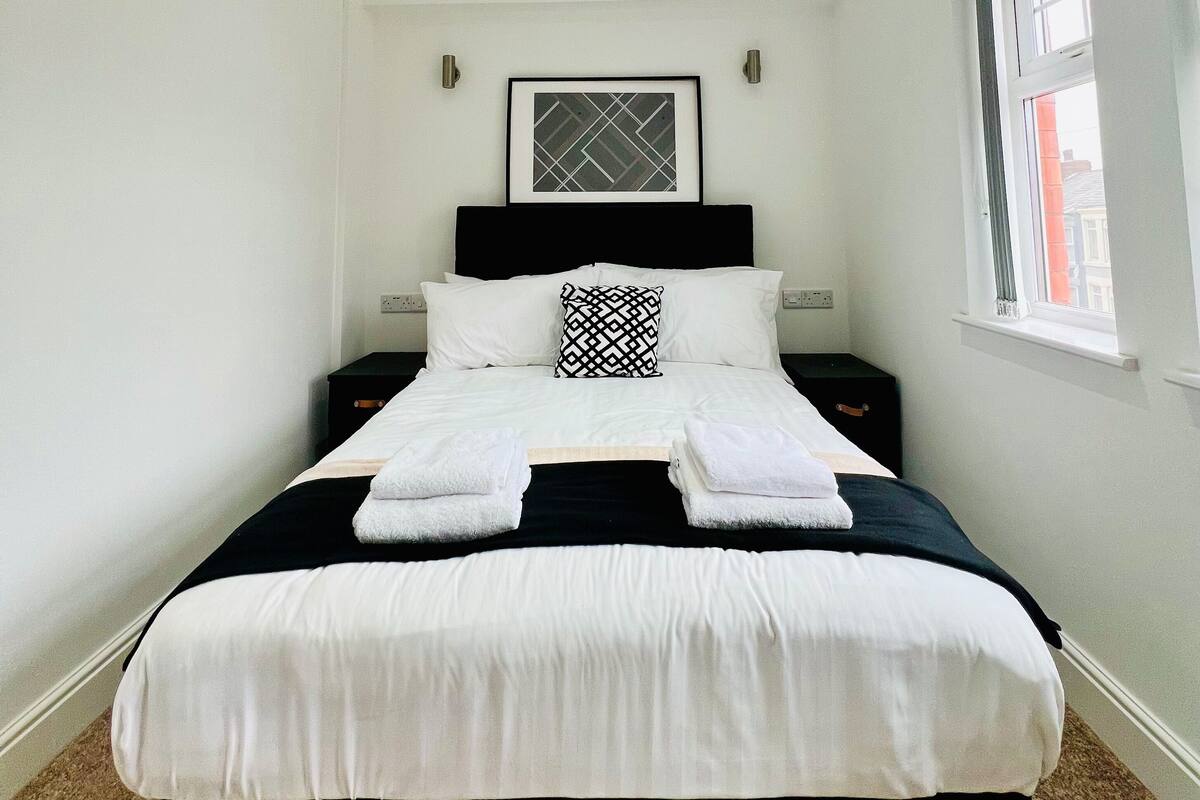 Una cama bien hecha con sábanas blancas, cabecera negra y almohada de estampado geométrico.