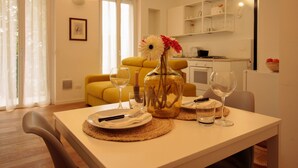 A dining area with a table set for two, a vase with flowers, and a kitchen in the background. - Italianway Easy - Caterina da Forlì 6 (Milan)