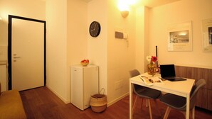 A compact living space with a dining area, a small refrigerator, a clock, and a wall-mounted light fixture. - Italianway Easy - Caterina da Forlì 6 (Milan)
