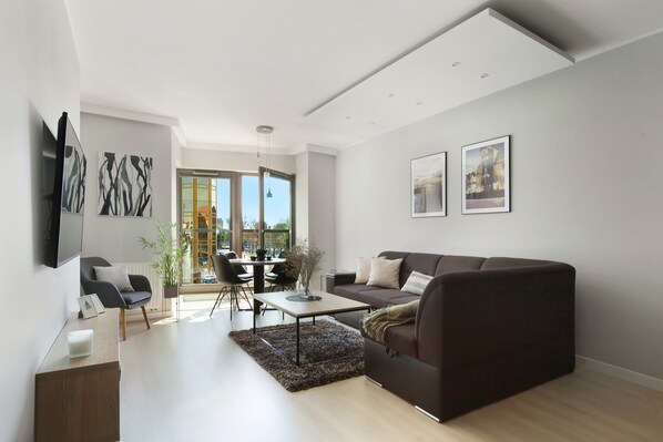 A modern living room with a sofa, coffee table, and a dining area with chairs and a table.