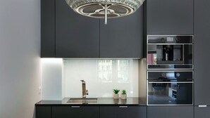 A modern kitchen with a built-in oven, a stainless steel range hood, and a pendant light above the counter. - Elite Apartments Waterlane SPA (Gdansk)