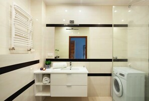 A modern bathroom with a white vanity, a glass shower enclosure, and a built-in washing machine.