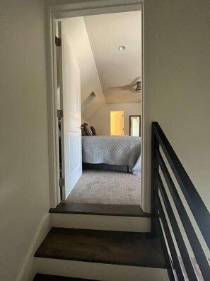 Staircase leads to a cozy bedroom with a bed, ceiling fan, and door to another room.