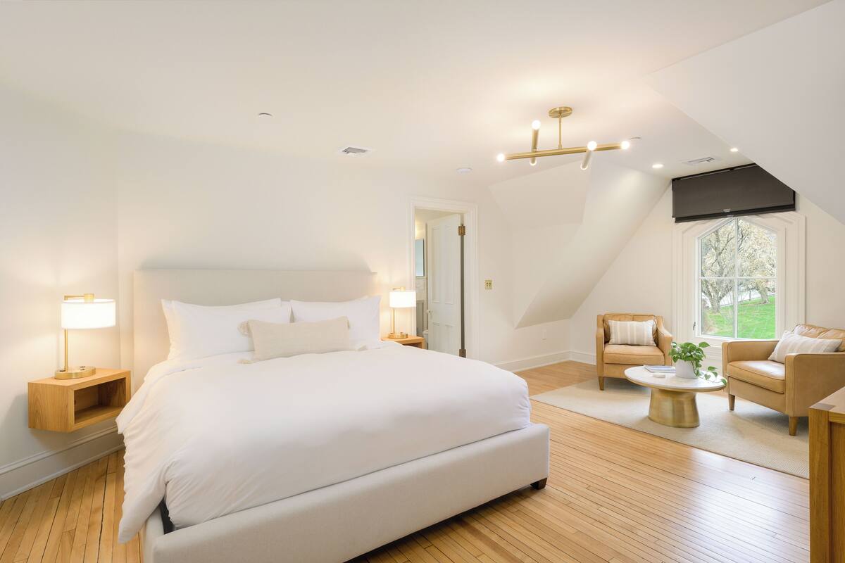 Un dormitorio moderno con una cama grande, una zona de estar con una mesita de centro y vistas a un jardín por la ventana.