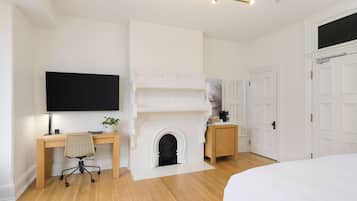 A bedroom with a wooden desk, a chair, a fireplace, a bed, and white doors.