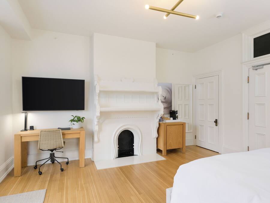 A bedroom with a wooden desk, a chair, a fireplace, a bed, and white doors.