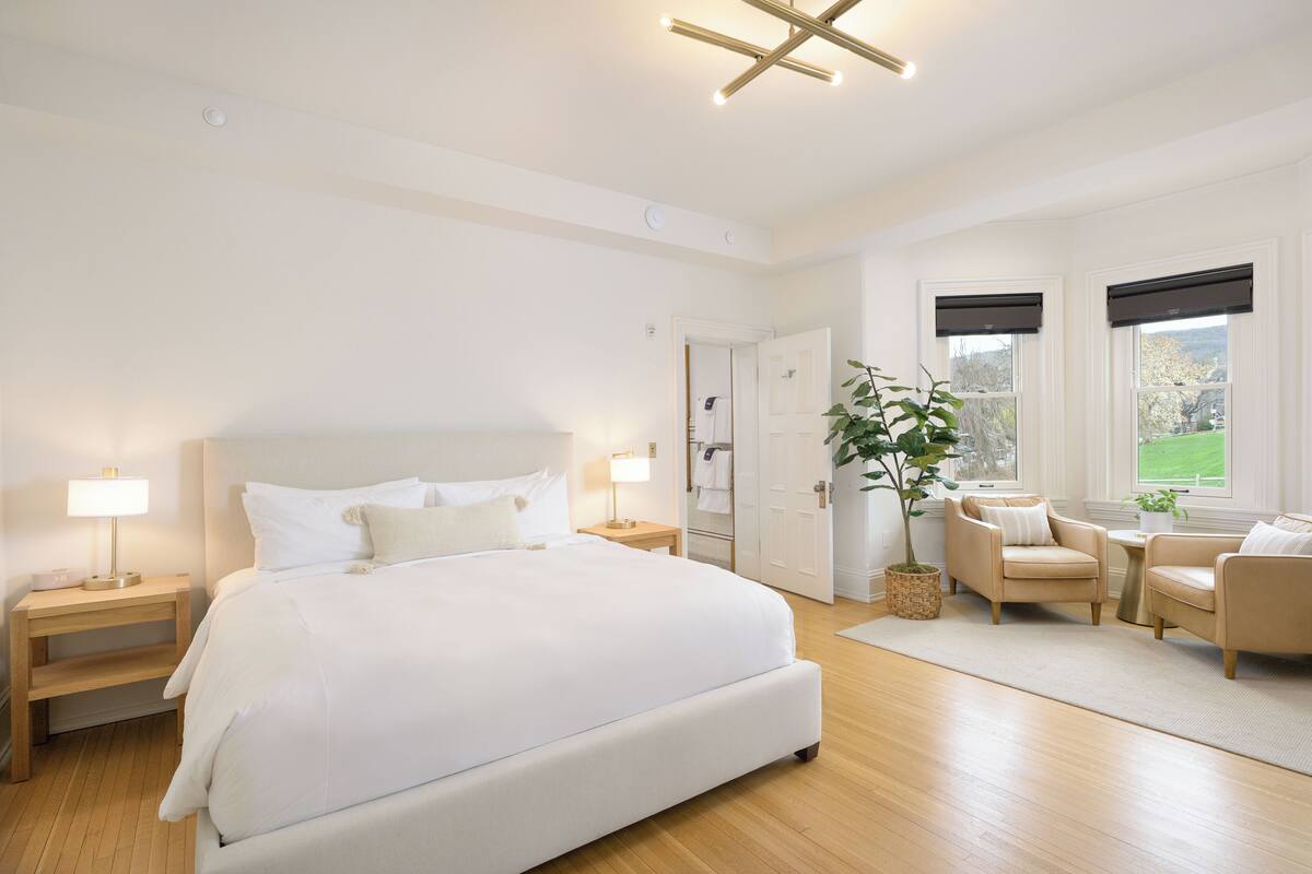 Un dormitorio moderno con una cama grande, mesitas de noche, una zona de estar con dos sillones y una planta en maceta.