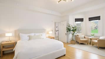 Un dormitorio moderno con una cama grande, mesitas de noche, una zona de estar con dos sillones y una planta en maceta.