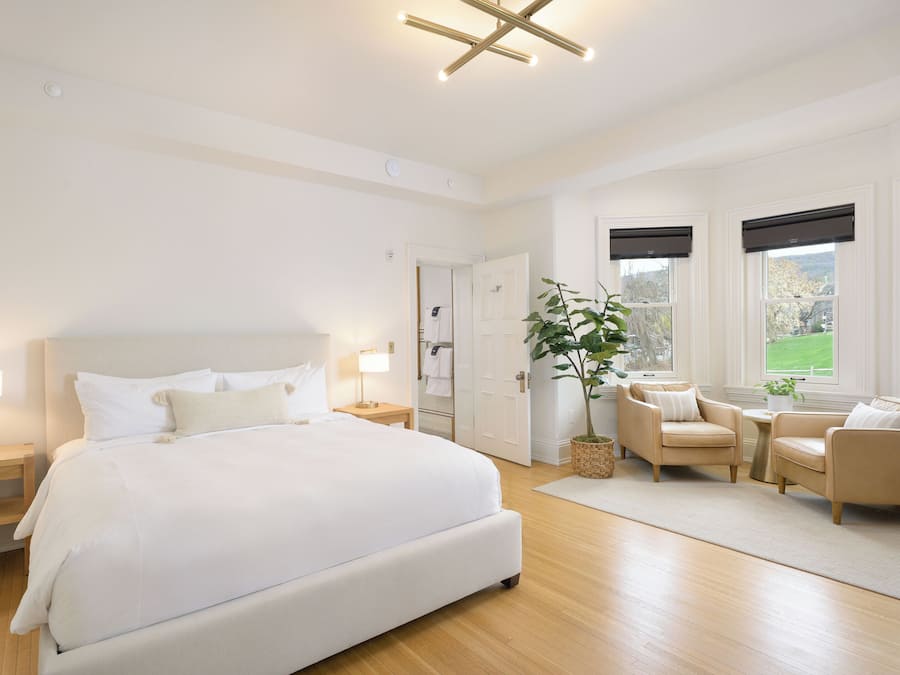 Un dormitorio moderno con una cama grande, mesitas de noche, una zona de estar con dos sillones y una planta en maceta.