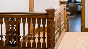 A wooden staircase with ornate balusters and a handrail, leading to a room with a wooden ceiling and a chandelier. - Wilbur Mansion (Bethlehem)