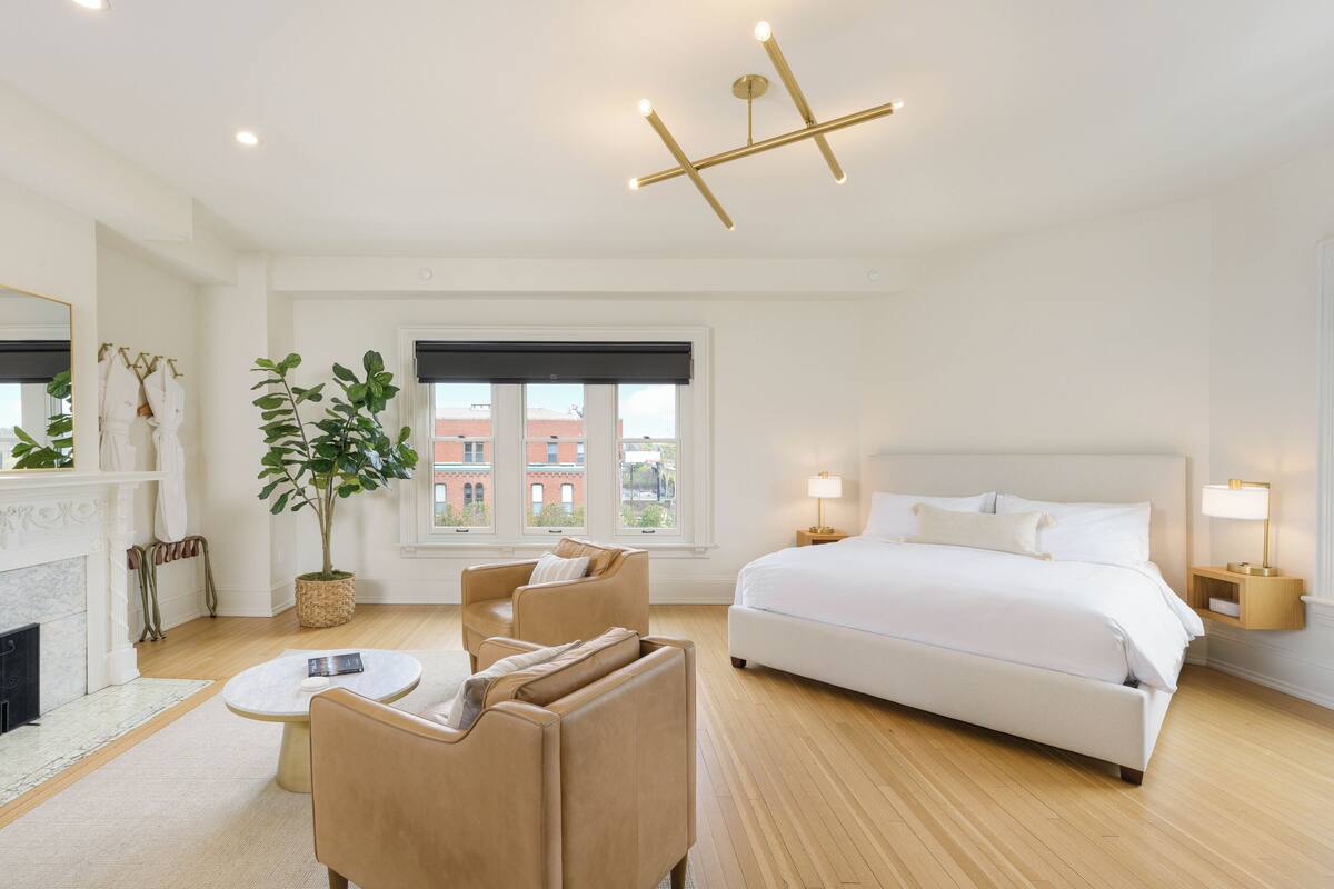 Una habitación de hotel moderna con una cama grande, un área de descanso con una mesa, una chimenea y vistas a la ciudad.