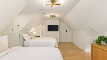 A modern bedroom with two beds, a wooden floor, and a ceiling light fixture.