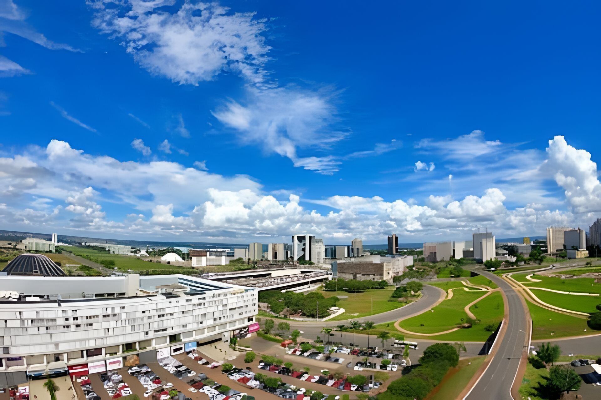 A modern building with a parking lot and a road curving through a green landscape.