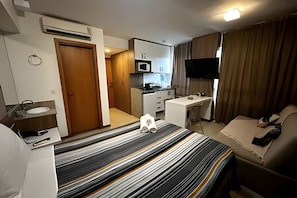 A hotel room with a bed, a desk, a TV, a bathroom, and a kitchenette. - Saint Moritz com vista espetacular de Brasilia (Brasília)