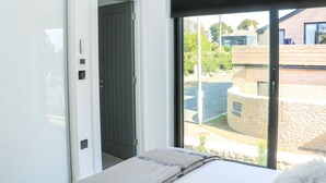 A bedroom with a bed, a window, and a door leading to a hallway. - Sail Loft (Dawlish)