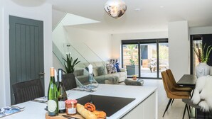 A modern kitchen with a central island, dining area, and a view of the outdoor patio. - Sail Loft (Dawlish)
