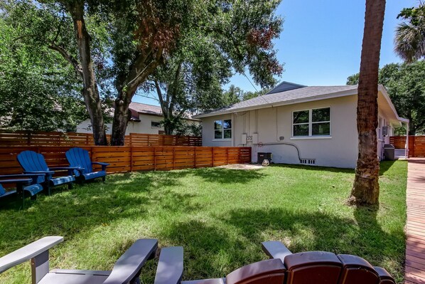 A backyard with a house, a wooden fence, and blue chairs.