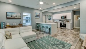 A modern living room with a white sofa, a green patterned rug, and a ceiling fan.