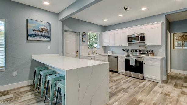 A modern kitchen with white cabinets, a central island, and bar stools.
