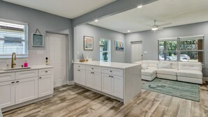 A modern kitchen with white cabinetry, a large island, and a dining area with a white sofa.