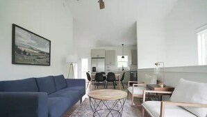 A modern living room with a blue sofa, a round coffee table, and a dining area with a table and chairs.