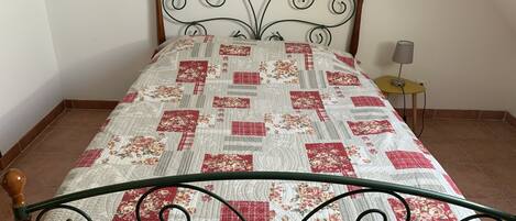 Una cama con colcha floral, cabecera de madera y mesita de noche con lámpara.