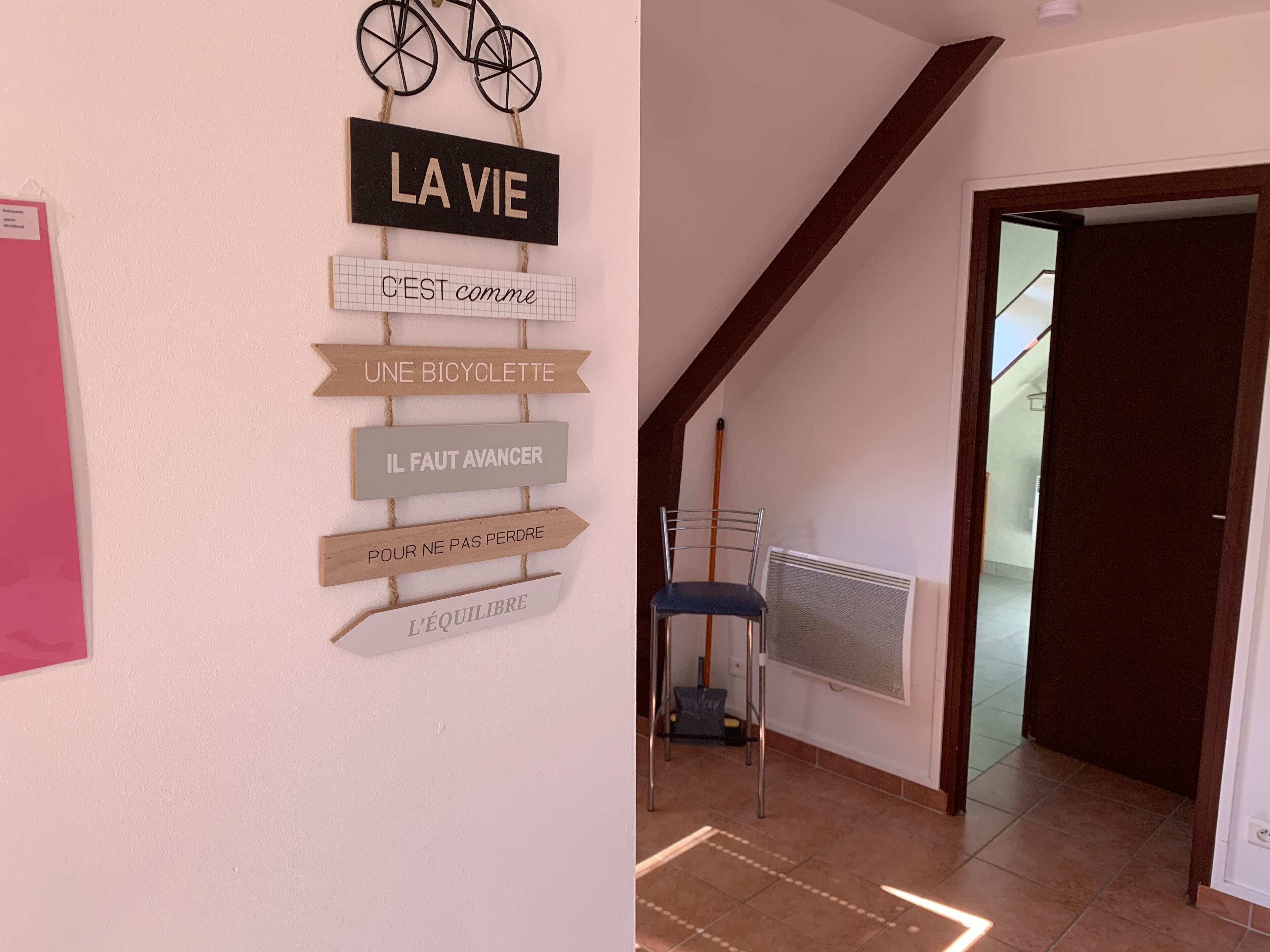 Eine Wand mit französischen Schildern, ein Fahrrad und ein Stuhl in einem Raum mit schrägverlaufender Decke und Heizkörper.