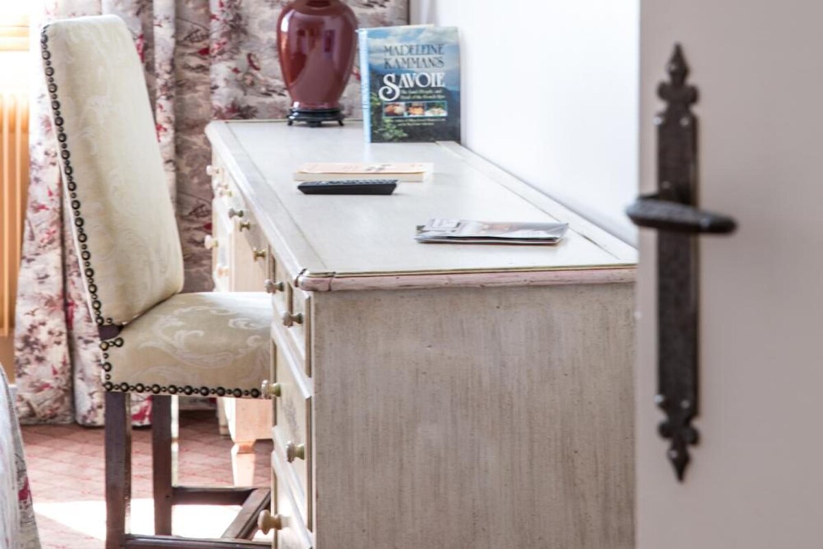 A room with a desk, a chair, a lamp, a book, and a mirror on the wall.