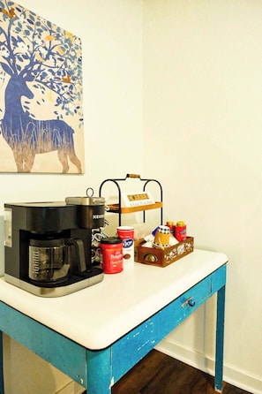 A coffee maker, Folgers coffee, and a mug on a table with a blue drawer.