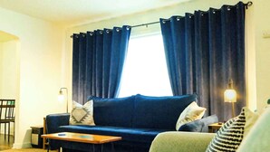 A living room with a blue sofa, a green sofa, a small table, and a lamp. - Aurora Loft | 2BR | ORV Trail 2 + Iron Belle (Ironwood)