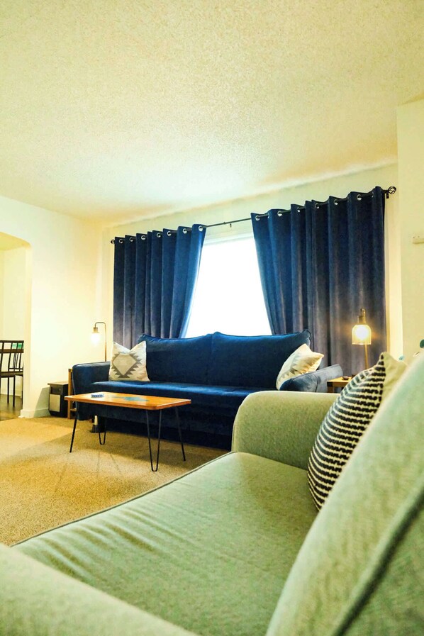 A living room with a blue sofa, a green sofa, a small table, and a lamp.