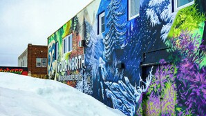 A building with a colorful mural depicting a snowy landscape and a sign that reads "YOUR NORTH Where adventure begins." - Aurora Loft | 2BR | ORV Trail 2 + Iron Belle (Ironwood)