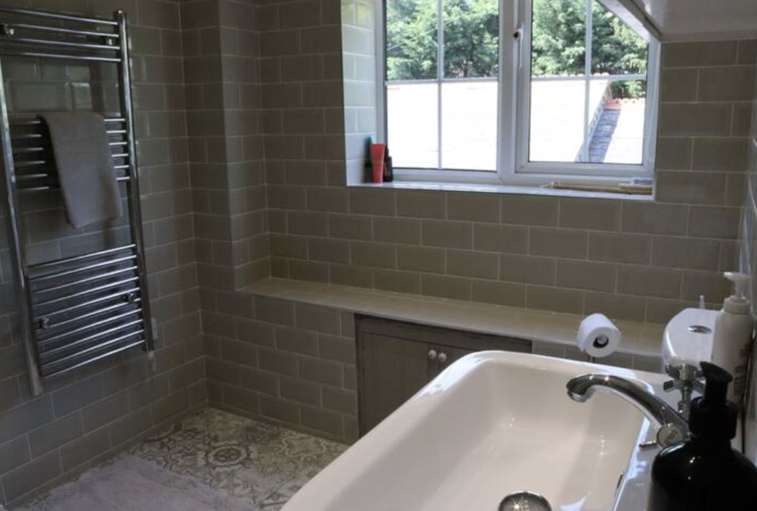 Un baño con lavamanos, toallero, ventana y dispensador de papel higiénico.