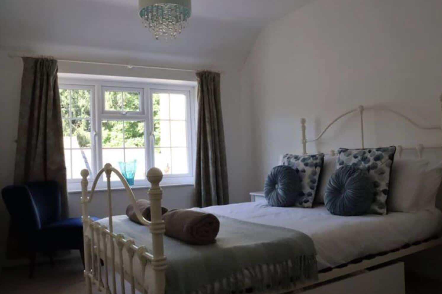Een slaapkamer met een bed, een stoel, een raam met gordijnen en een kroonluchter.