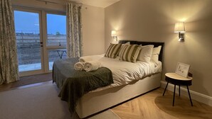 Een slaapkamer met een bed, een nachtkastje, een lamp en uitzicht op het strand door een glazen deur.