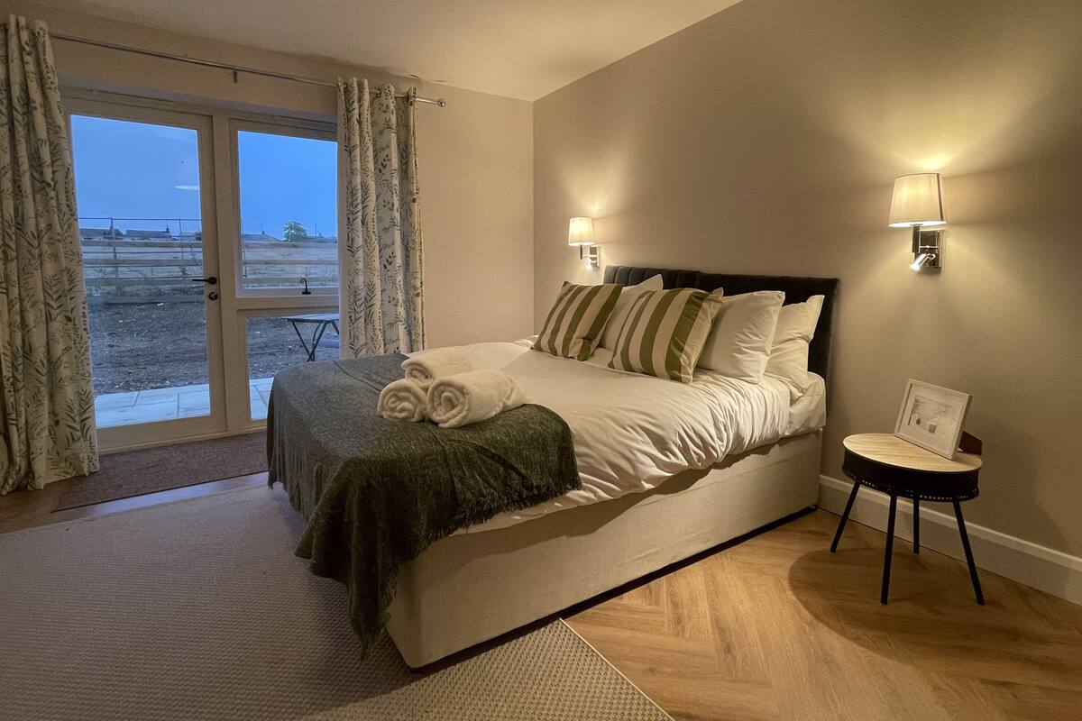 Ein Schlafzimmer mit einem Bett, einem Nachttisch, einer Lampe und Blick auf den Strand durch eine Glastür.