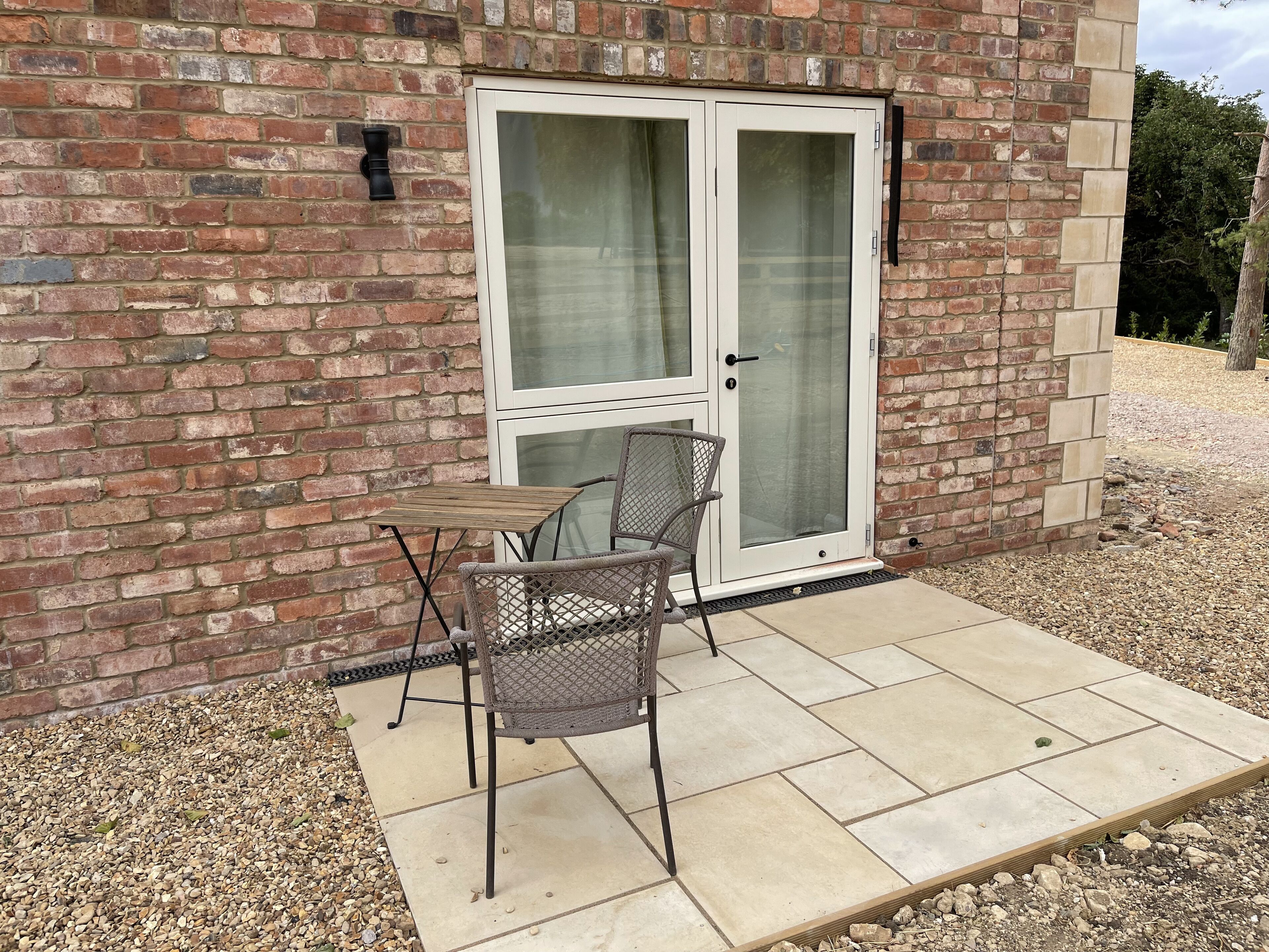 A patio with a table and chairs, a sliding glass door, and a brick wall.