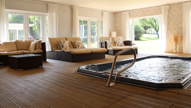 Een ruime binnenruimte met een jacuzzi, meerdere zithoeken en grote ramen voor natuurlijk licht.