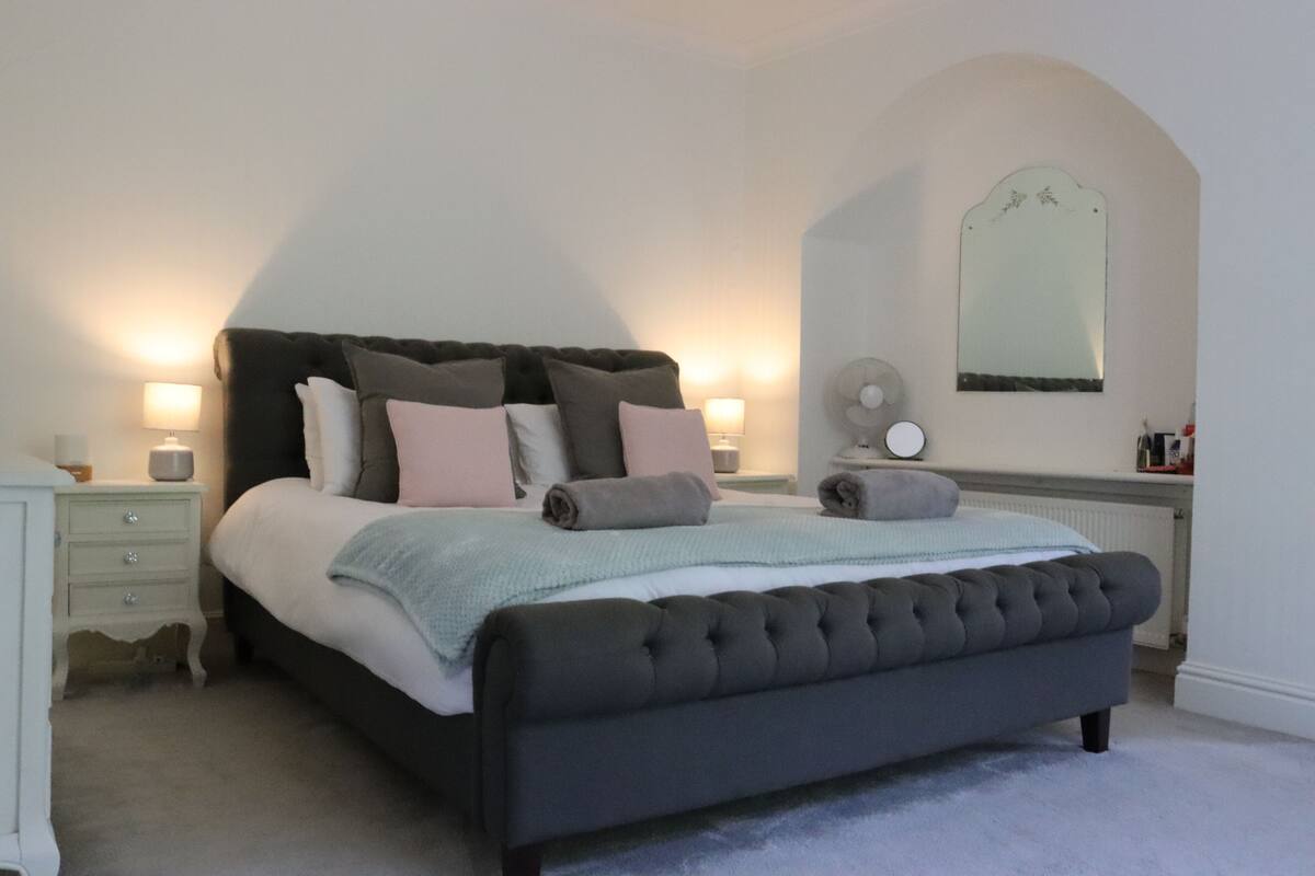 Ein Schlafzimmer mit einem großen Bett, Nachttischlampen, einem Spiegel und einem Schminktisch.
