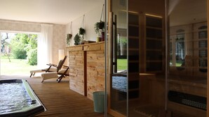 Een wellnessruimte met een jacuzzi, houten vloeren, een zithoek met stoelen en een glazen deur naar een zwembad.