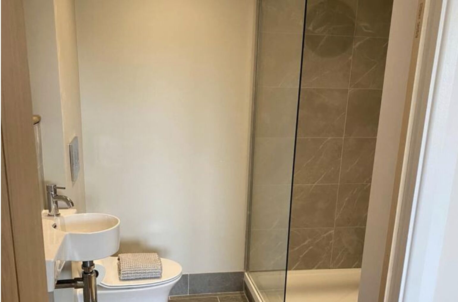 A modern bathroom with a white sink, a towel, and a glass shower enclosure.