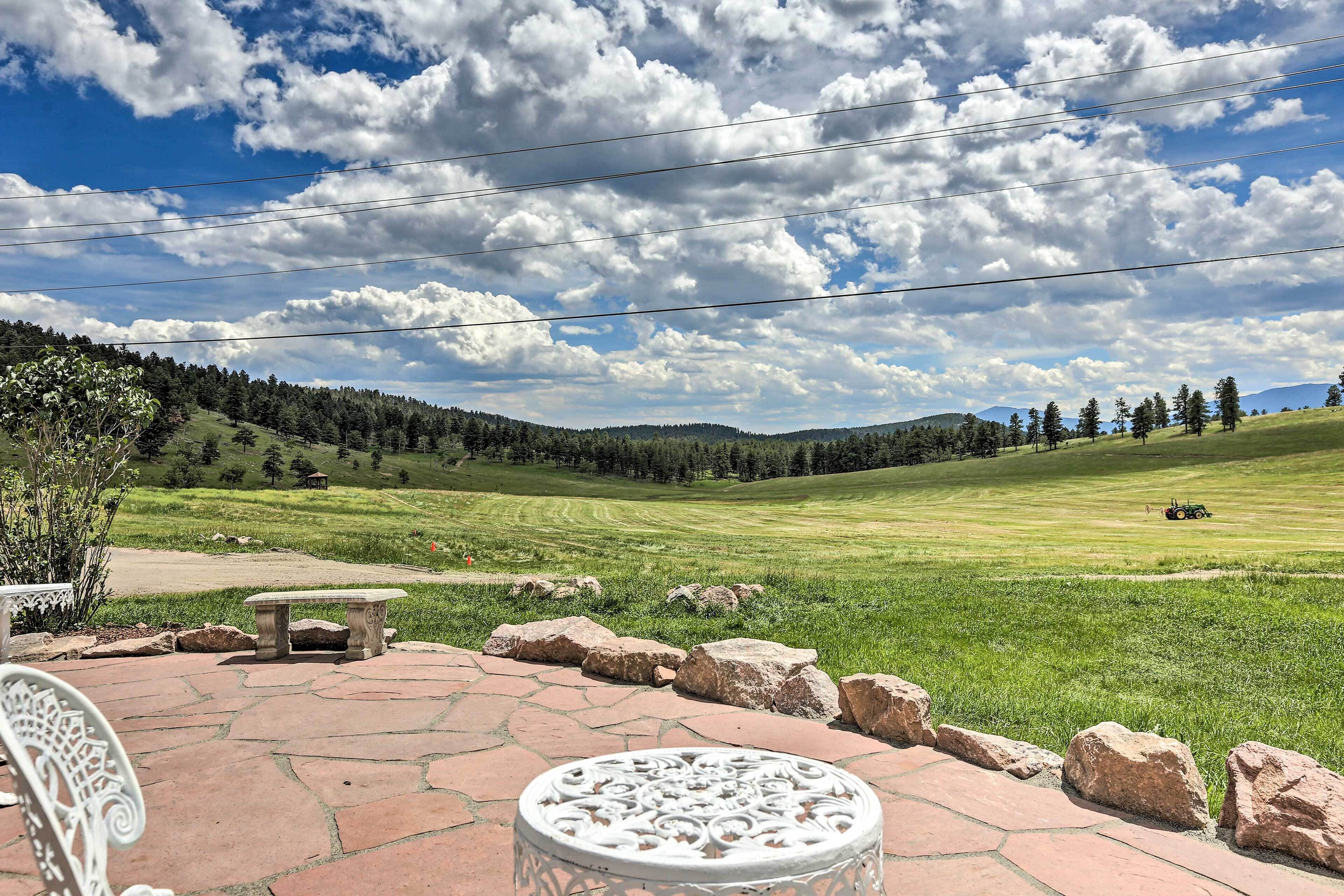 A patio with a stone table and bench, overlooking a grassy field with a tractor.