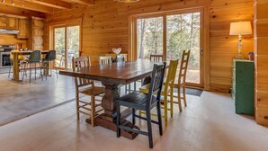 A wooden cabin interior with a dining table, chairs, a kitchen area, and large windows. - L'Anse 750 sur la rivière Sacacomie (Saint-Alexis-des-Monts)