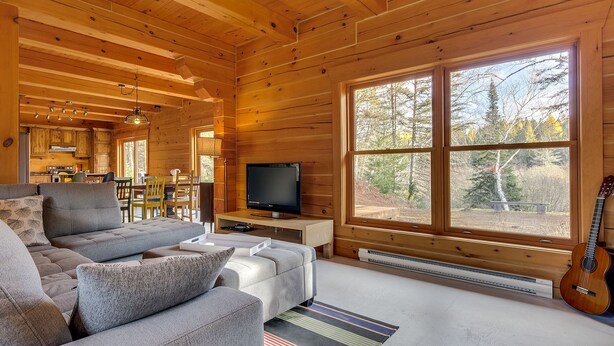 A cozy cabin interior with a wooden interior, a sofa, a television, and a guitar. - L'Anse 750 sur la rivière Sacacomie (Saint-Alexis-des-Monts)