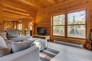 Een gezellig chaletinterieur met houten inrichting, een bank, een televisie en een gitaar.