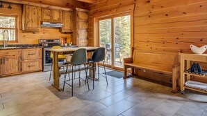 A wooden cabin kitchen with a central island, bar stools, and a dining table. - L'Anse 750 sur la rivière Sacacomie (Saint-Alexis-des-Monts)