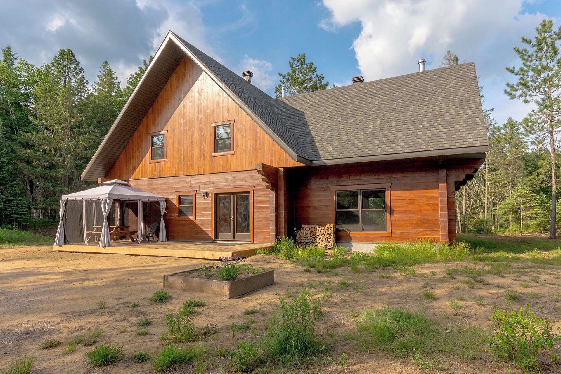 A wooden cabin with a large porch, a covered outdoor seating area, and a fire pit.