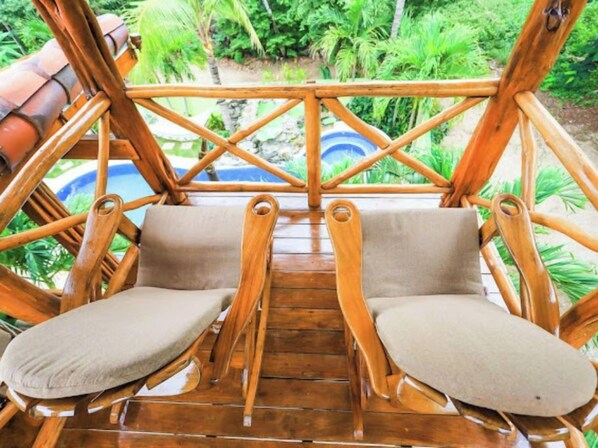 Terraza de madera con dos sillas acolchadas y barandilla de madera.